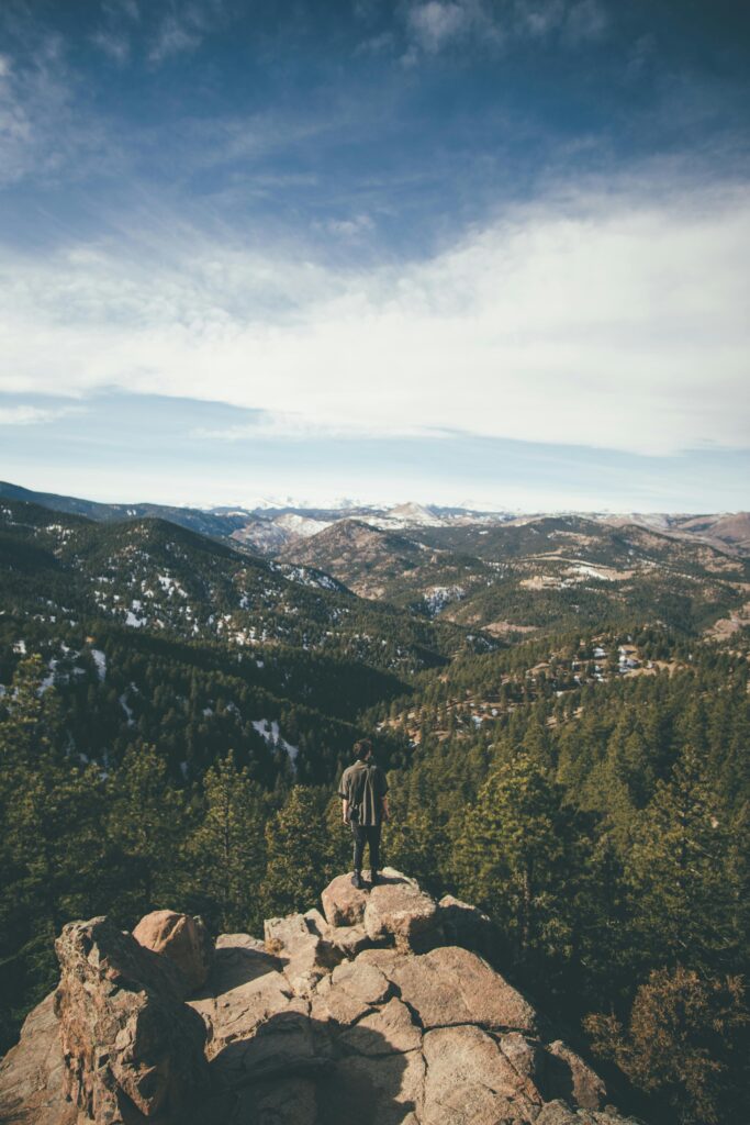 A hiker stands on a cliff edge enjoying a scenic view of Mountains outside of Loveland Colorado