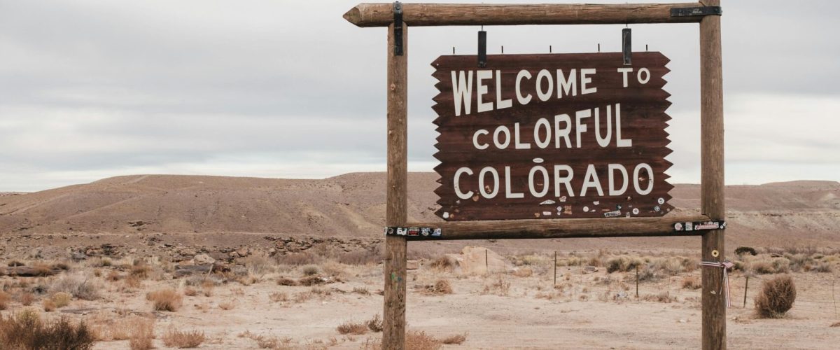 Desert scene with a Welcome to Colorful Colorado sign, overcast sky.